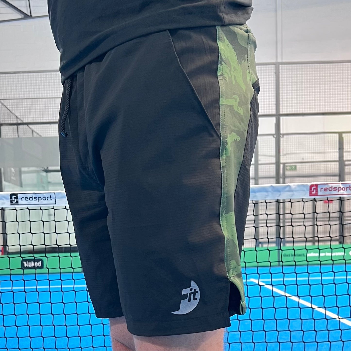 man wearing black shorts with a green stripe on a Padel court