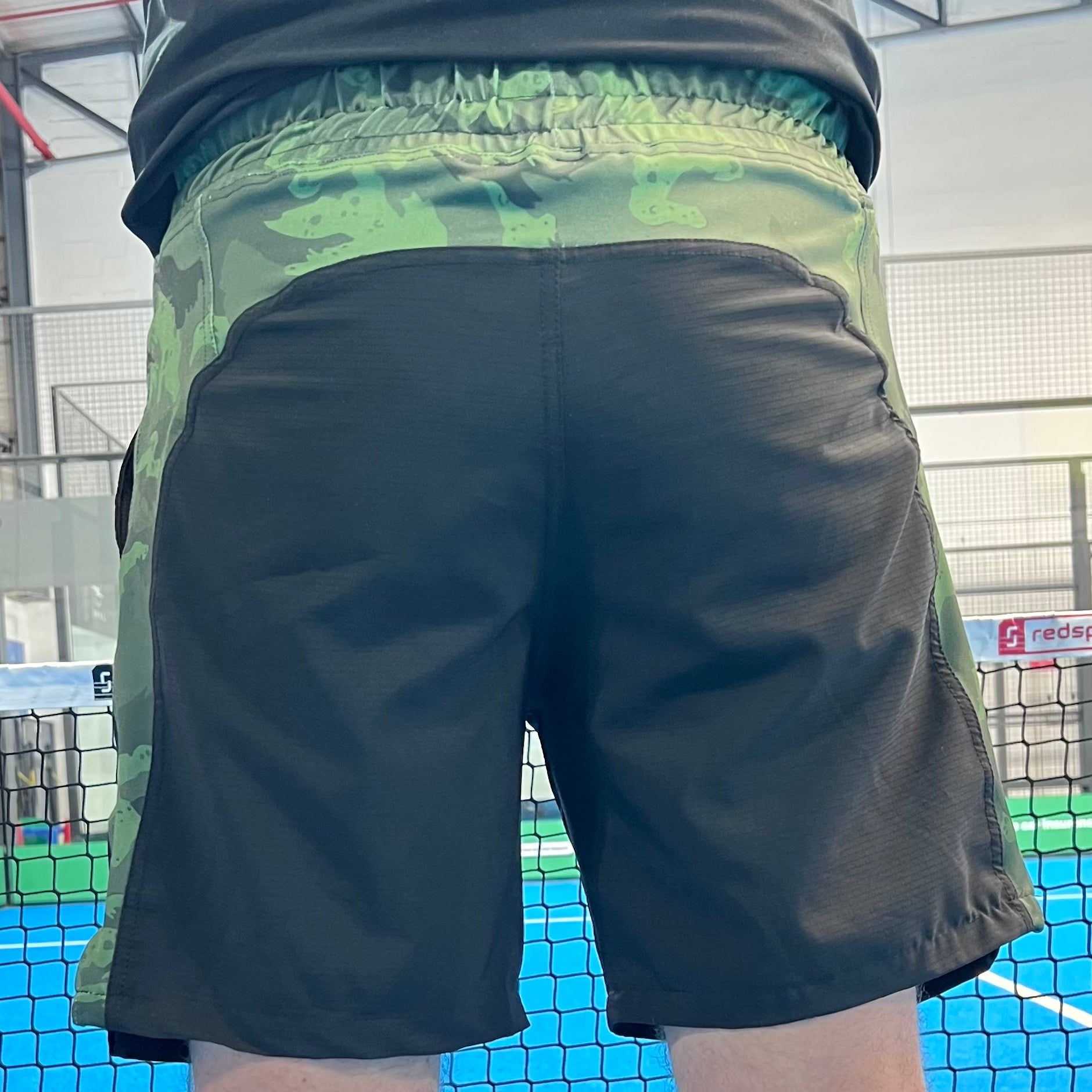 Person wearing black shorts with a camouflage pattern on a sports court.