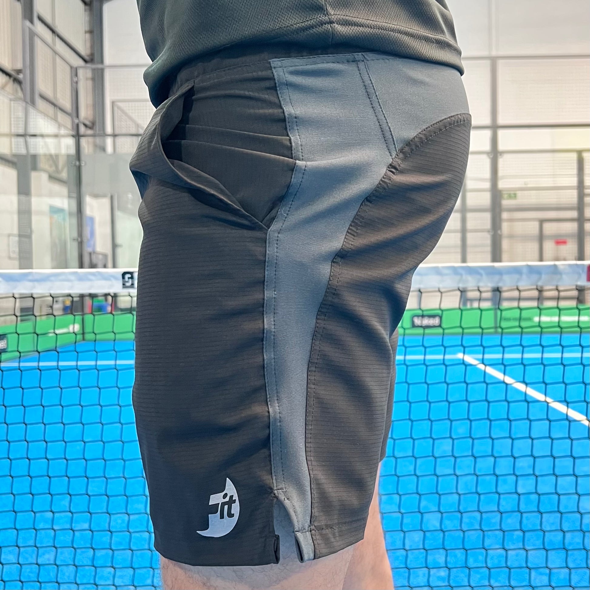Person wearing gray athletic shorts with a brand logo on a padel court.